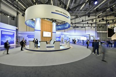 Messestand von Müller Martini auf der drupa 2024: runder Turm mit Logo-Ring, darunter Bildschirme und Besucher