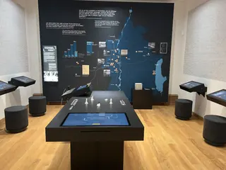 Medientisch mit Touchscreen und Touch-Stationen vor einer großformatigen Wandgrafik