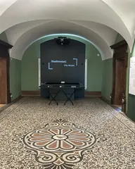 Gewölbegang mit Mosaikboden, an der Stirnwand eine Medienstation mit Projektor